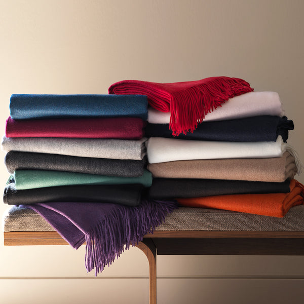 colorful cashmere throws styled in a stack on a bench.