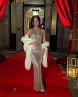 young female adult from bachelorette series wearing silver gown with white cashmere fur trimmed shawl over her shoulders standing on a red carpet