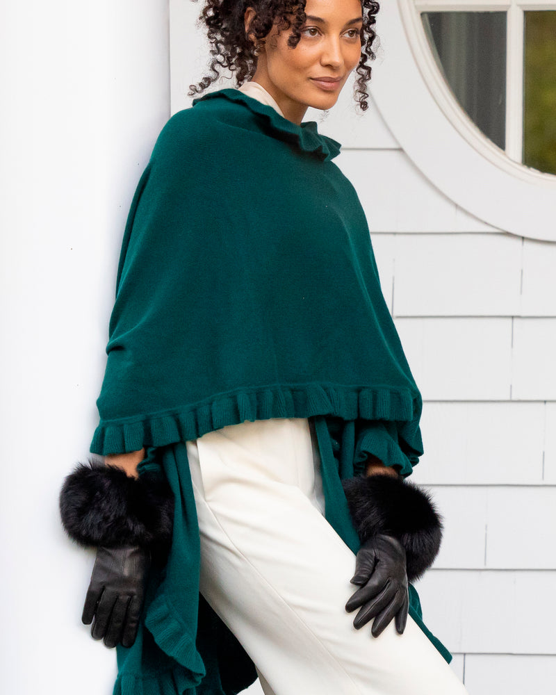 woman leaning on white pillar wearing volant ruffle cashmere cape in green and Mano fur trimmed leather glove in black